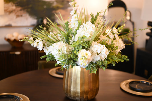 Neutral-toned dining table centerpiece featuring white calla lilies, tulips, and peonies in a golden bowl.