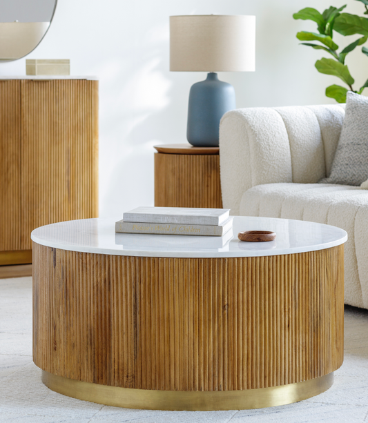Round mango wood coffee table with reeded base, gold trim on bottom, and a white marble top