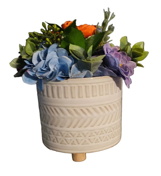 Decorative ceramic planter with artificial flowers on a wooden surface against a dark wall.