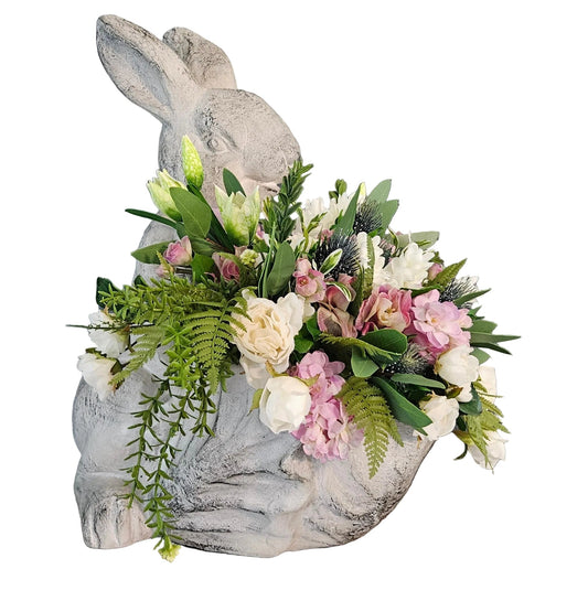 Decorative bunny figurine with floral arrangement against a gray wall with decorative text.