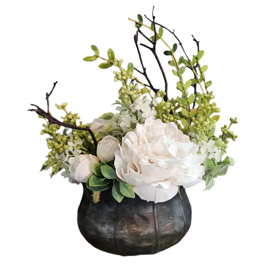 Decorative flower arrangement with white flowers and greenery in a black pumpkin-shaped container on a white background.