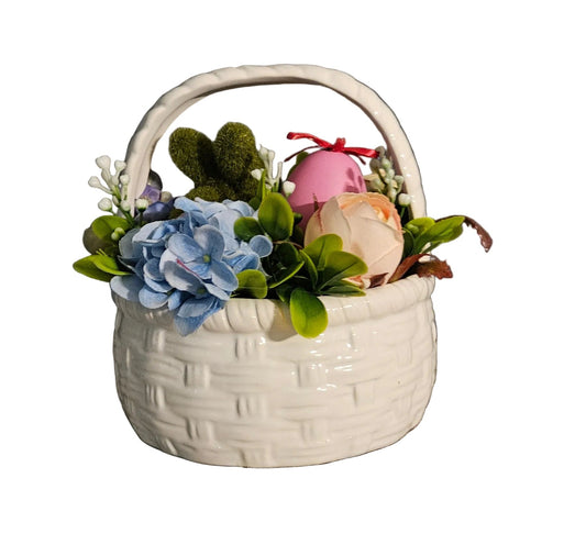 White woven basket with artificial flowers and eggs on a wooden surface against a dark wall.