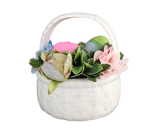 White woven basket with artificial flowers and a pink candle on a rustic wooden surface.