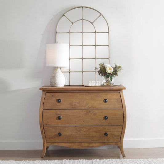 Wooden dresser with three drawers, a lamp, and flowers against a white wall.