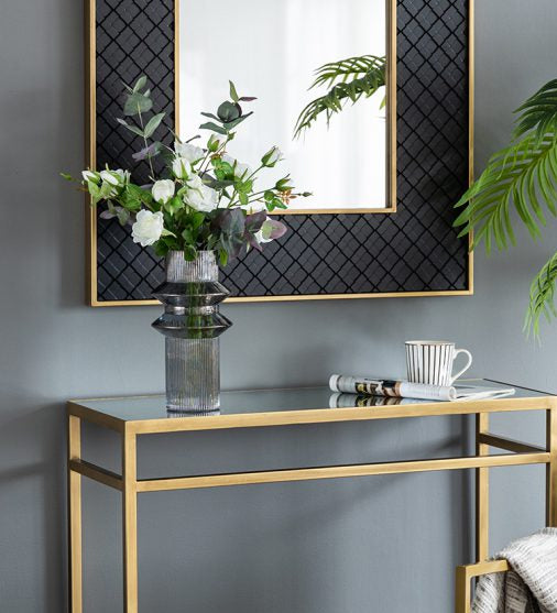 Modern interior with a gold console table, mirror, and chair against a gray wall.