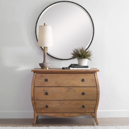 Wooden dresser with a lamp, plant, and books on top against a white wall.