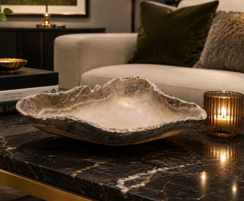 Decorative stone bowl on a marble surface with a candle and books in the background.