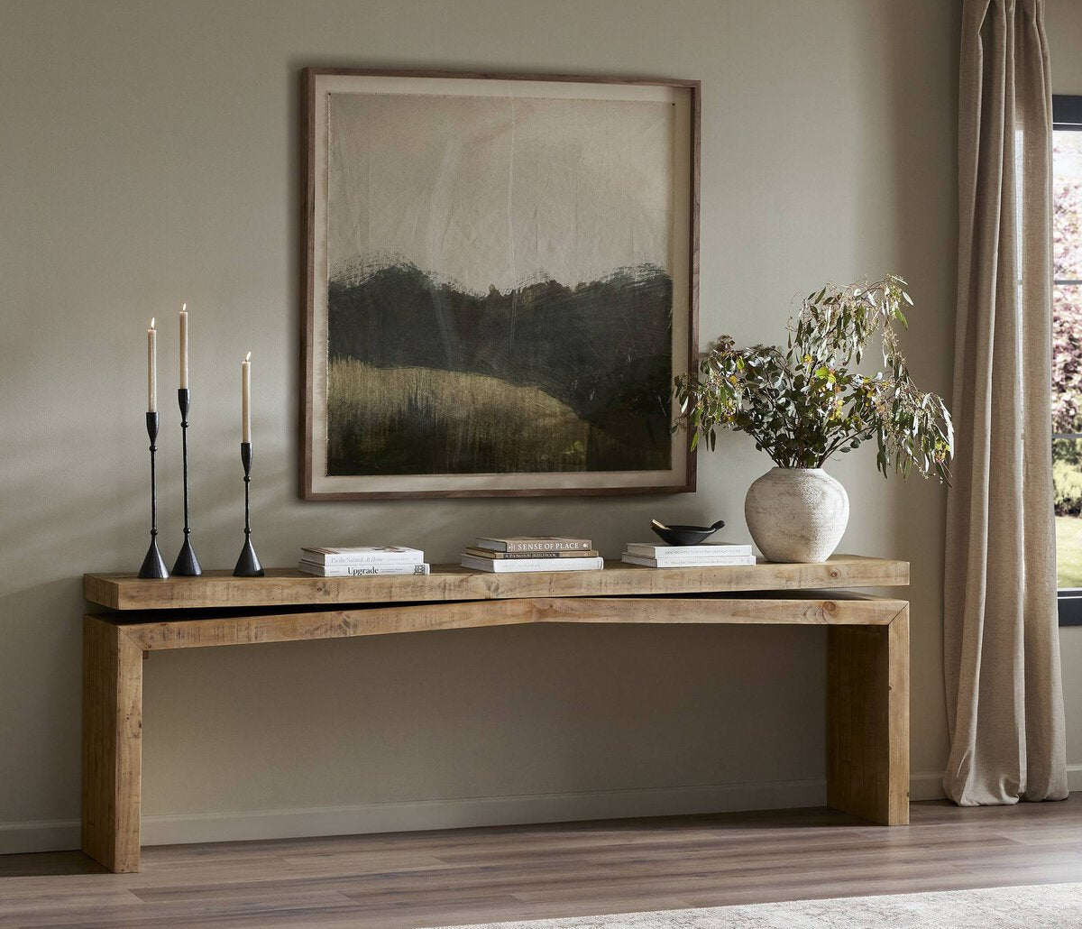 Wooden console table with decorative items against a wall with a framed abstract painting.
