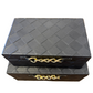 Two stacked black woven leather jewelry boxes with gold-tone chain handles, placed on a wooden tabletop.