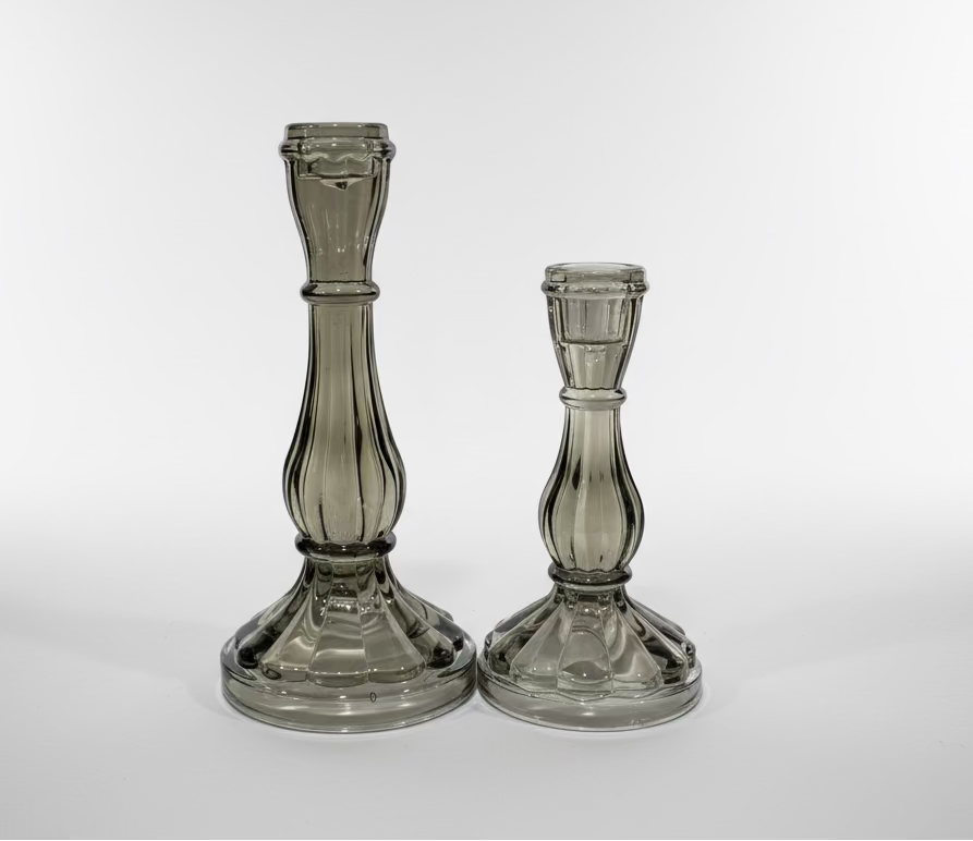 Two glass candle holders on a white surface with a pegboard background