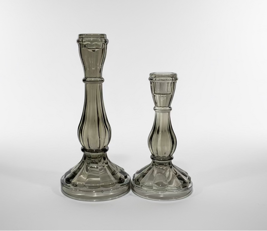 Two glass candle holders on a white surface with a pegboard background
