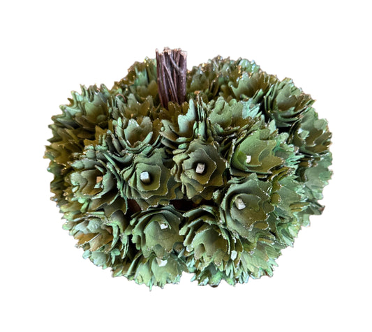 Decorative green pine cone ball on a wooden surface with a white textured background