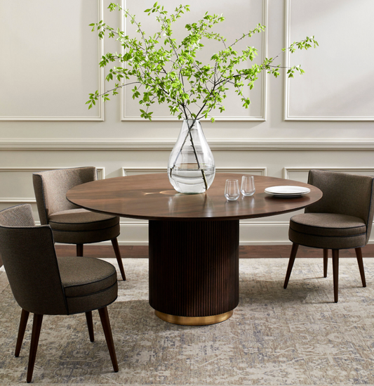 Dining room with a round wooden table and four chairs, featuring a vase with green branches.