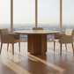 Modern dining room with a round table and chairs in front of large windows with a cityscape view.