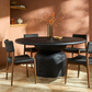 Dining room with a round dark wooden table and chairs against a warm-toned wall.