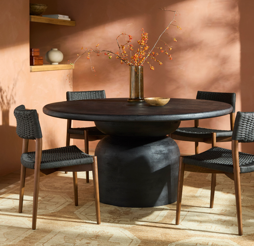 Dining room with a round dark wooden table and chairs against a warm-toned wall.