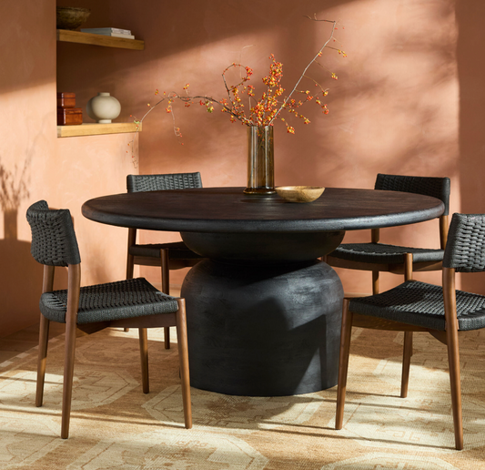 Dining room with a round dark wooden table and chairs against a warm-toned wall.