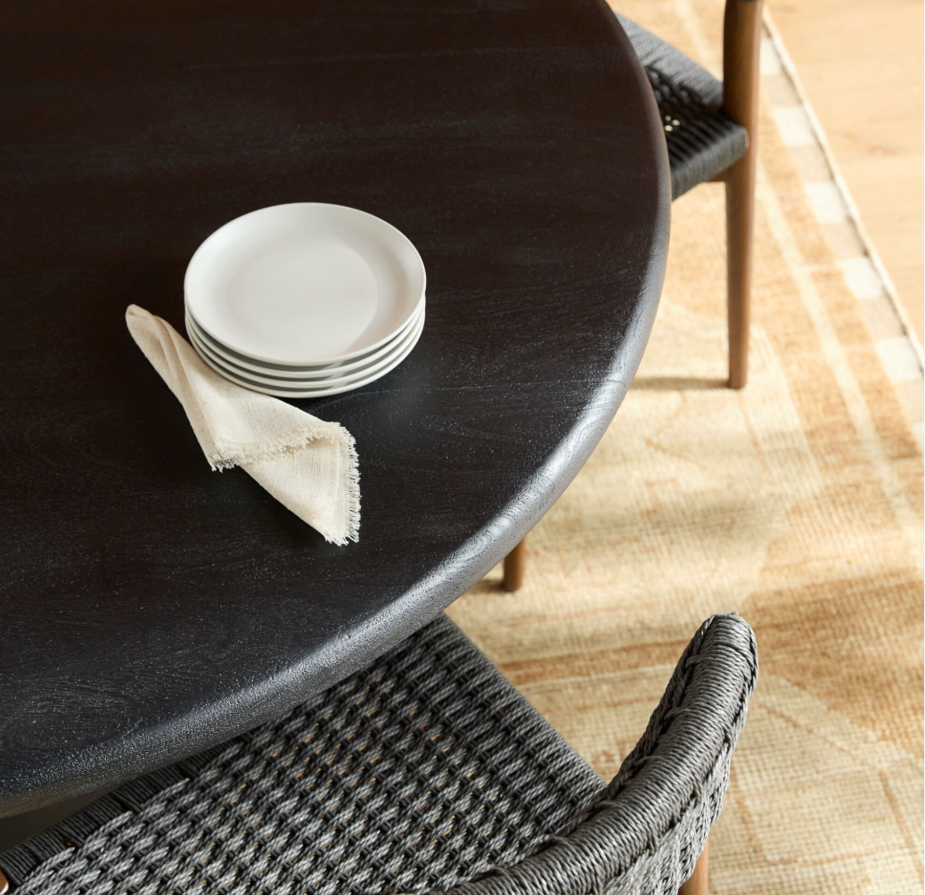 Round black table with white plates and a napkin on a wooden floor.