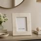 Beige picture frame with 'ELEVARRE' branding on a decorative shelf with a vase, books, and lamp.