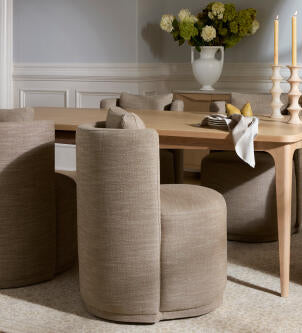 Dining room with wooden table and beige chairs, featuring a vase of flowers and candles.