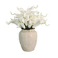 White artificial flowers in a textured vase on a wooden surface with a gray wall background