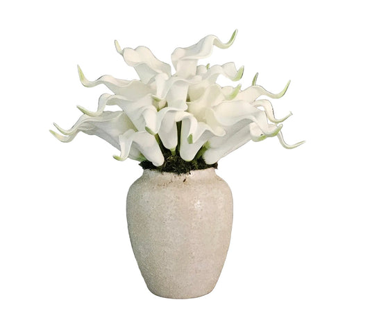 White artificial flowers in a textured vase on a wooden surface with a gray wall background
