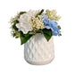 White textured vase with artificial flowers on a wooden surface against a gray wall