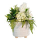 White textured vase with green and white flowers on a wooden surface against a dark wall