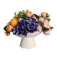Floral arrangement in a white ceramic container on a wooden surface with a gray wall background
