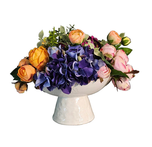 Floral arrangement in a white ceramic container on a wooden surface with a gray wall background