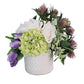 Floral arrangement with green, purple, and white flowers in a white vase on a white background
