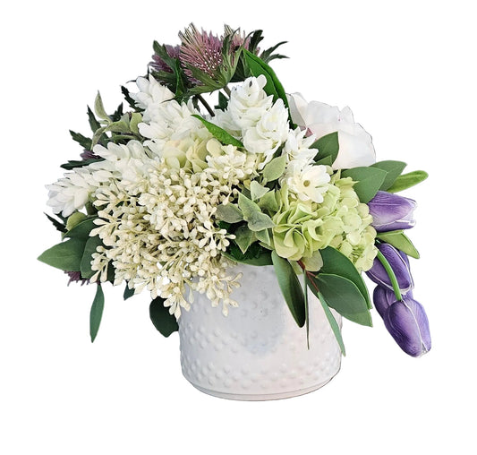Floral arrangement in a white vase on a wooden surface with a gray wall background